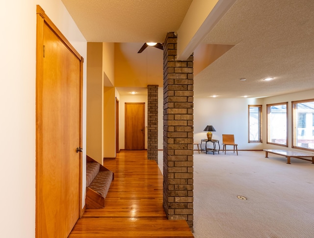 corridor featuring light wood finished floors, stairway, a textured ceiling, and ornate columns