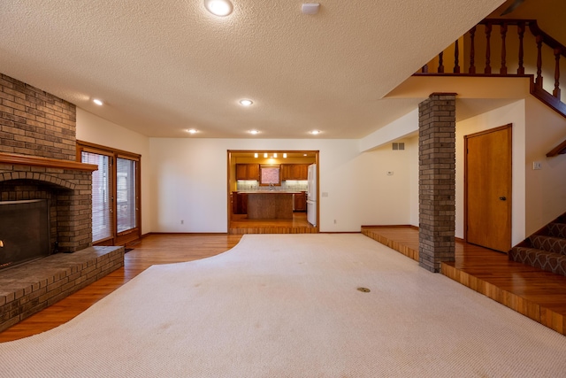 unfurnished living room featuring visible vents, a textured ceiling, a fireplace, stairs, and ornate columns