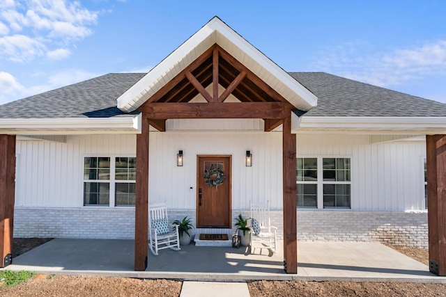 property entrance with brick siding, covered porch, and a shingled roof