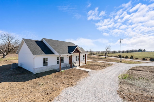 modern farmhouse style home featuring gravel driveway, central AC, and a shingled roof