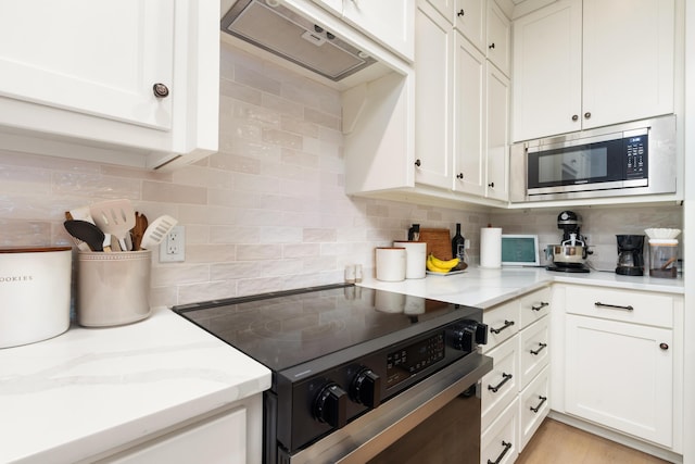 kitchen featuring tasteful backsplash, stainless steel microwave, light stone countertops, under cabinet range hood, and electric range oven