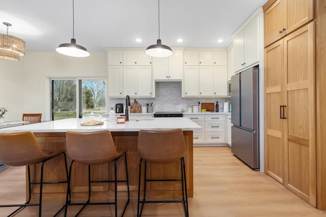 kitchen with light wood-style flooring, freestanding refrigerator, light countertops, a kitchen bar, and backsplash