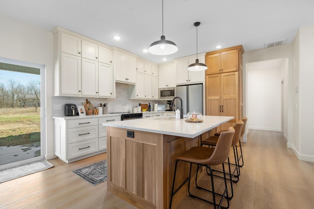 kitchen featuring visible vents, light countertops, decorative backsplash, light wood-style floors, and stainless steel appliances