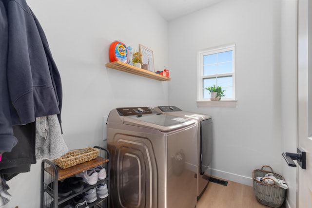 clothes washing area with laundry area, washing machine and dryer, light wood-type flooring, and baseboards