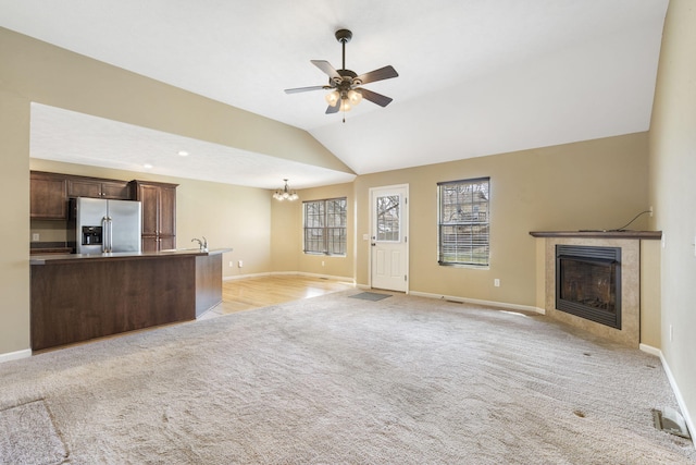 unfurnished living room featuring vaulted ceiling, baseboards, a tile fireplace, and light carpet