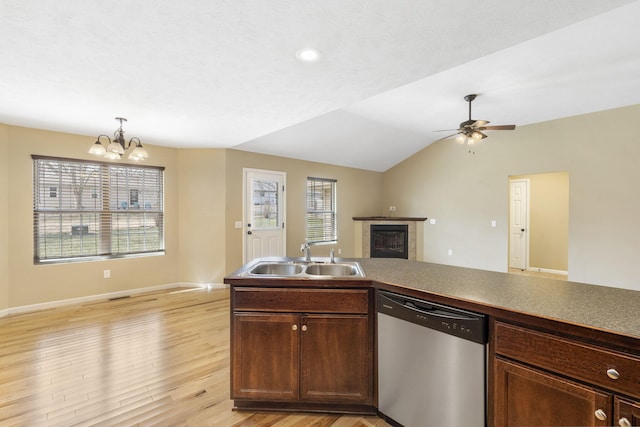 kitchen featuring a glass covered fireplace, a sink, vaulted ceiling, light wood-style floors, and stainless steel dishwasher