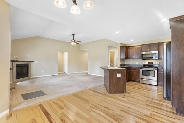 kitchen featuring dark countertops, open floor plan, a fireplace, stainless steel appliances, and a sink