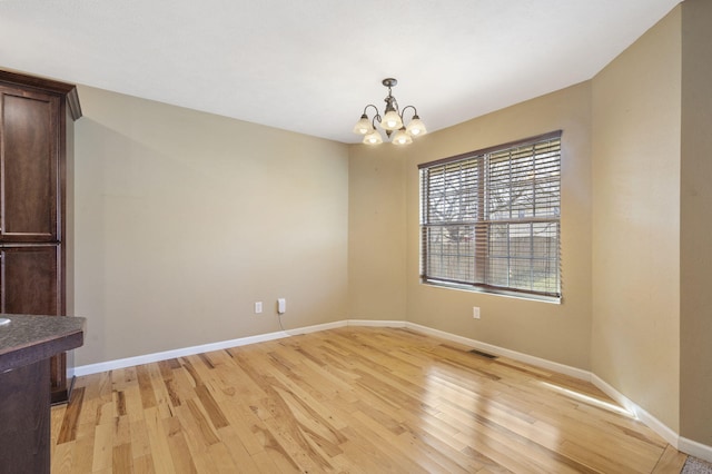 unfurnished dining area with a notable chandelier, visible vents, baseboards, and light wood-style floors