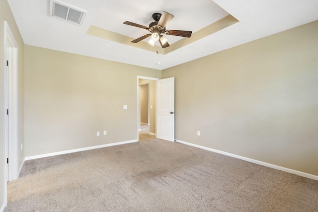 carpeted spare room featuring a tray ceiling, baseboards, visible vents, and ceiling fan