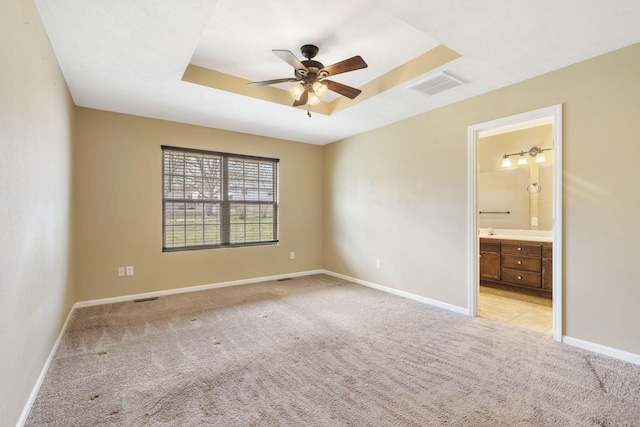 unfurnished bedroom with baseboards, a tray ceiling, light carpet, and visible vents