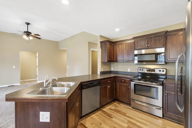 kitchen with a sink, dark countertops, stainless steel appliances, a peninsula, and light wood finished floors