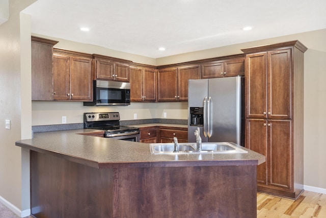 kitchen with a peninsula, light wood-style flooring, a sink, stainless steel appliances, and dark countertops