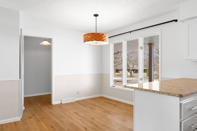 unfurnished dining area with a wainscoted wall, light wood-style floors, visible vents, and baseboards