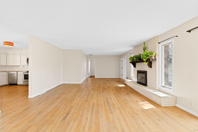 unfurnished living room with a brick fireplace, baseboards, and light wood-type flooring