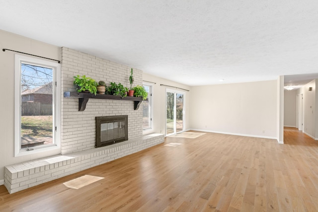 unfurnished living room with light wood-type flooring, baseboards, a textured ceiling, and a fireplace