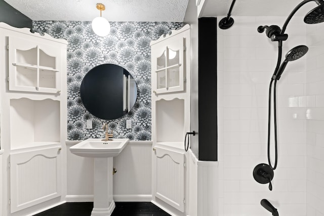 full bath featuring wallpapered walls, a textured ceiling, wood finished floors, and wainscoting