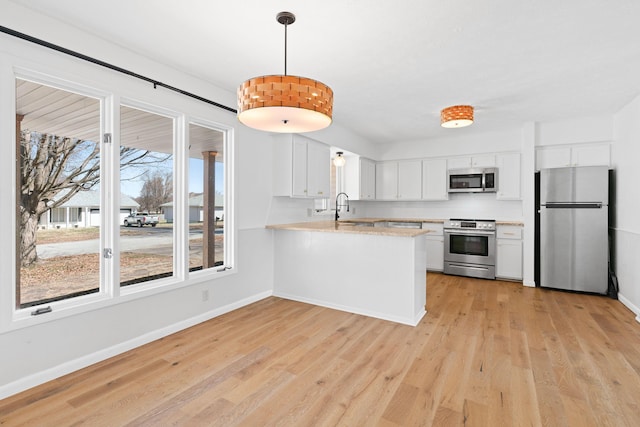 kitchen with a sink, appliances with stainless steel finishes, a peninsula, and light wood finished floors