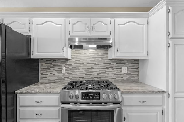 kitchen with tasteful backsplash, under cabinet range hood, freestanding refrigerator, white cabinets, and gas stove