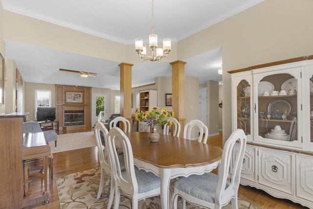 dining area featuring crown molding, a large fireplace, decorative columns, wood finished floors, and a ceiling fan