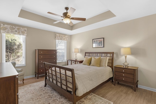 bedroom featuring a ceiling fan, a raised ceiling, wood finished floors, and baseboards