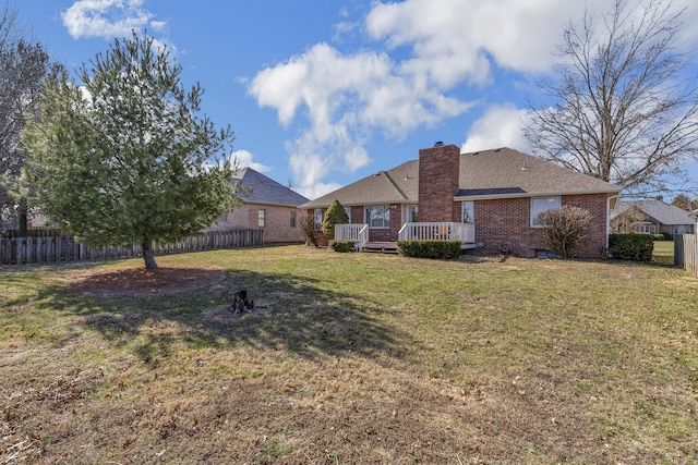 back of property featuring a deck, fence, a yard, brick siding, and a chimney