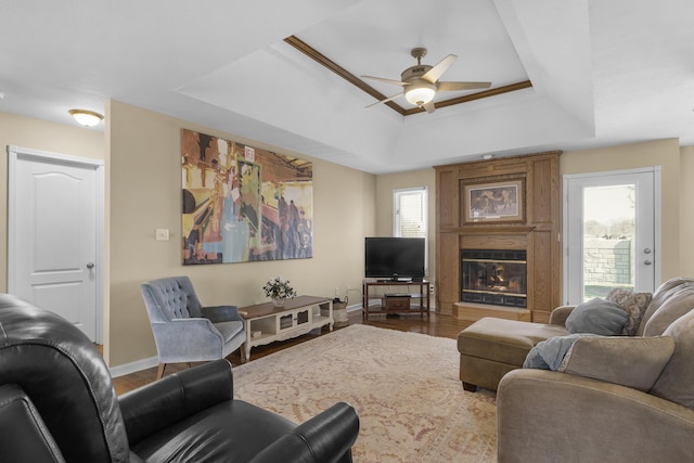 living room featuring wood finished floors, baseboards, a fireplace, ceiling fan, and a raised ceiling