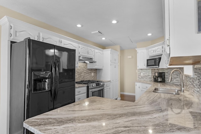 kitchen featuring under cabinet range hood, gas range, light stone counters, black fridge, and a sink