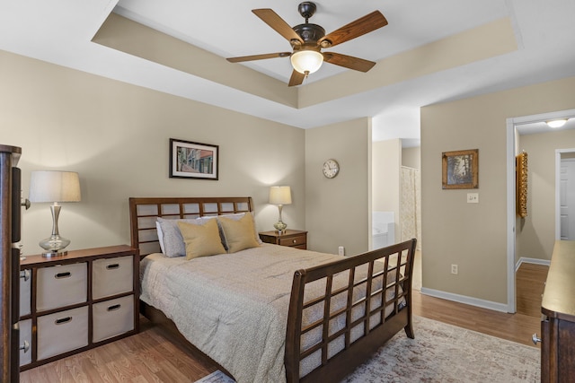 bedroom with a ceiling fan, a tray ceiling, wood finished floors, and baseboards