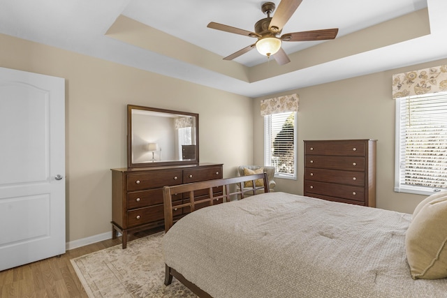 bedroom featuring baseboards, a ceiling fan, a tray ceiling, and wood finished floors