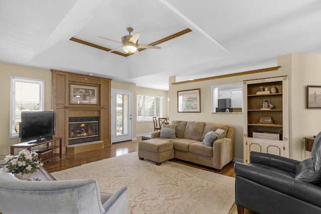 living area featuring a ceiling fan, a tray ceiling, wood finished floors, and a large fireplace