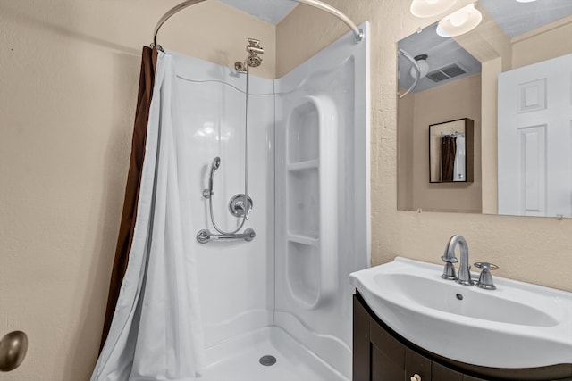 bathroom featuring vanity, a shower stall, a textured wall, and visible vents