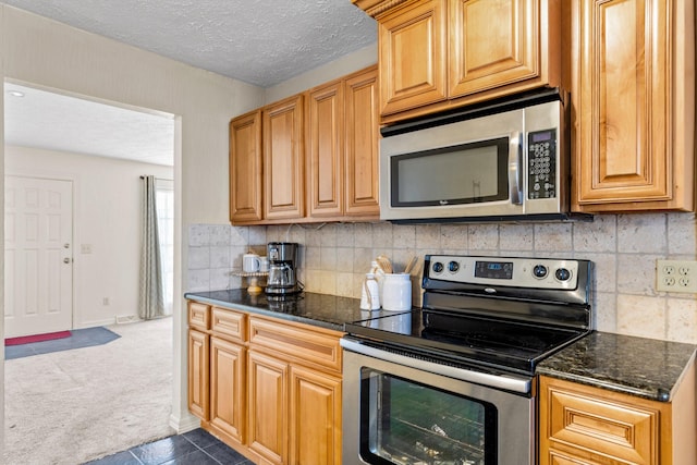 kitchen with dark stone counters, decorative backsplash, appliances with stainless steel finishes, a textured ceiling, and carpet flooring