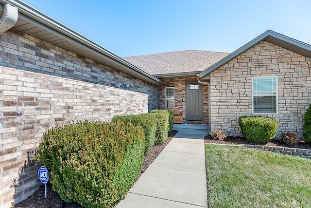 doorway to property featuring brick siding and roof with shingles