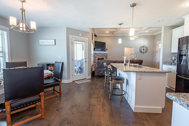 kitchen featuring a sink, fridge with ice dispenser, a fireplace, white cabinetry, and dark wood-style flooring