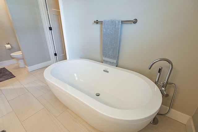 full bathroom with tile patterned flooring, toilet, baseboards, and a freestanding tub