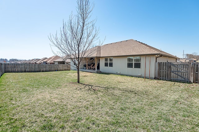 rear view of house with a yard, roof with shingles, and a fenced backyard