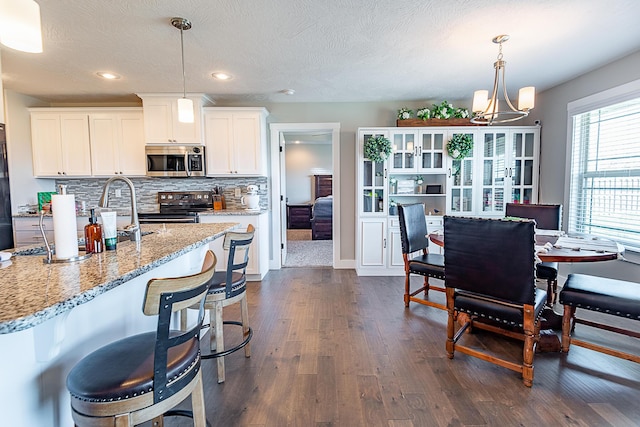 kitchen featuring a sink, light stone counters, backsplash, dark wood finished floors, and appliances with stainless steel finishes