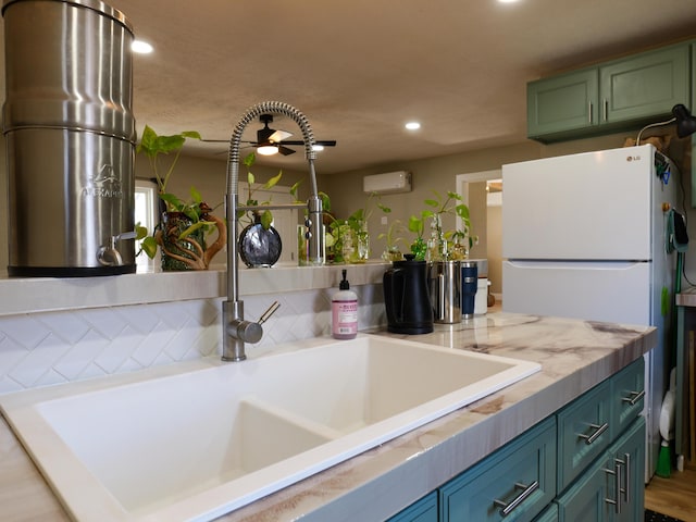 kitchen with green cabinets, an AC wall unit, recessed lighting, freestanding refrigerator, and a sink