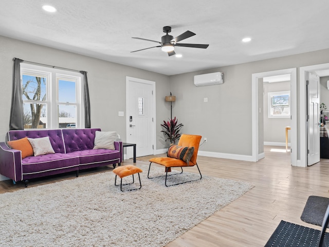 living area featuring a wealth of natural light, baseboards, light wood-style floors, and a wall unit AC