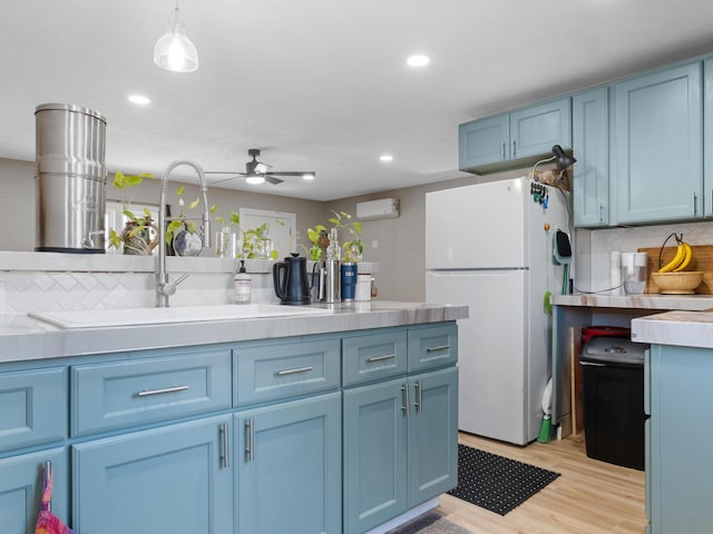 kitchen featuring blue cabinetry, a sink, tasteful backsplash, freestanding refrigerator, and light wood finished floors