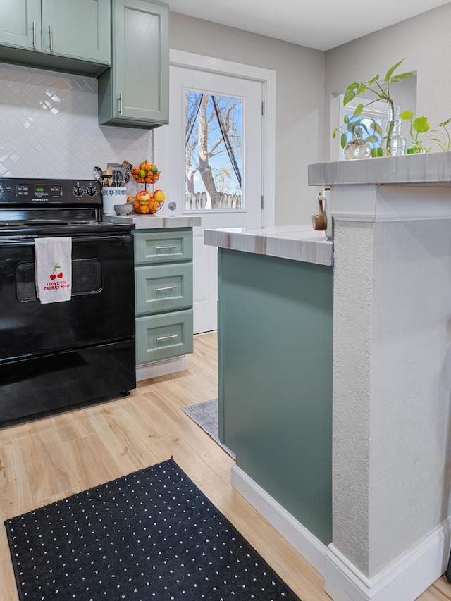 kitchen featuring black / electric stove, baseboards, green cabinets, light wood-type flooring, and backsplash