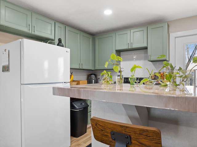 kitchen featuring green cabinets, backsplash, light wood-style floors, and freestanding refrigerator