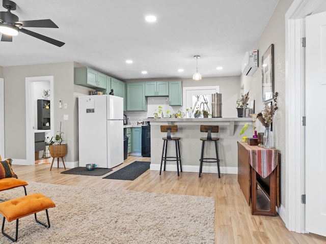 kitchen featuring a wall unit AC, a breakfast bar area, freestanding refrigerator, light wood-style floors, and green cabinets