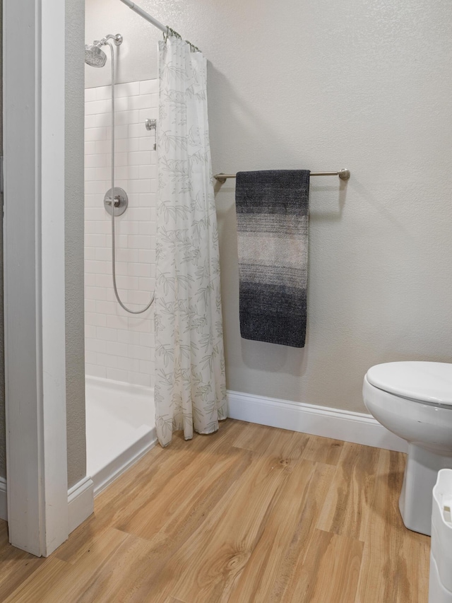 full bathroom featuring a stall shower, toilet, baseboards, and wood finished floors