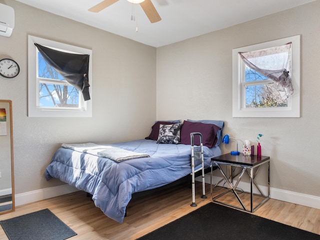 bedroom with ceiling fan, a wall mounted AC, baseboards, and wood finished floors