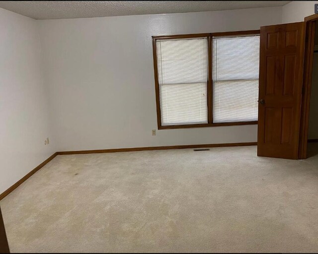 spare room with baseboards, visible vents, and light carpet