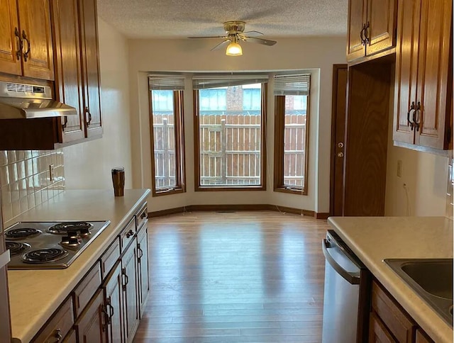 kitchen featuring stainless steel appliances, light countertops, light wood-style floors, under cabinet range hood, and a textured ceiling