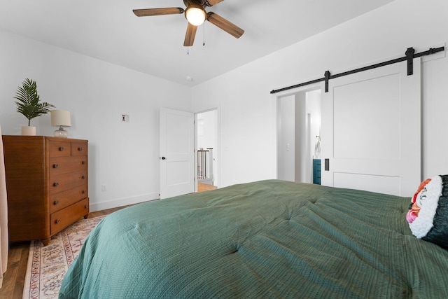 bedroom with ceiling fan, a barn door, baseboards, and wood finished floors