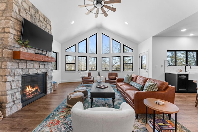 living room with light wood finished floors, a stone fireplace, recessed lighting, and high vaulted ceiling