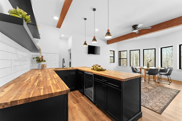 kitchen with wine cooler, beamed ceiling, dark cabinets, wood counters, and a sink